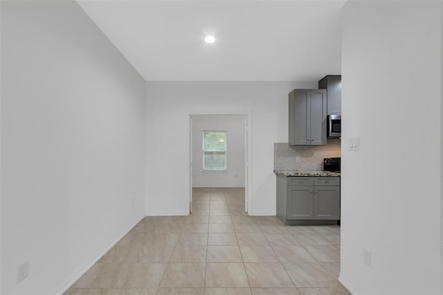 kitchen featuring light tile patterned floors, baseboards, gray cabinets, stainless steel microwave, and backsplash