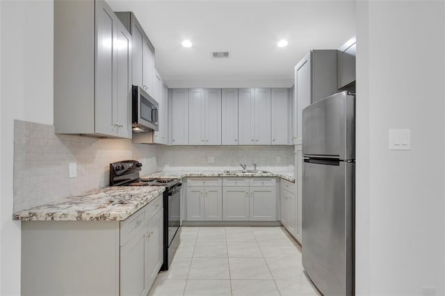 kitchen featuring tasteful backsplash, light stone counters, light tile patterned flooring, stainless steel appliances, and a sink