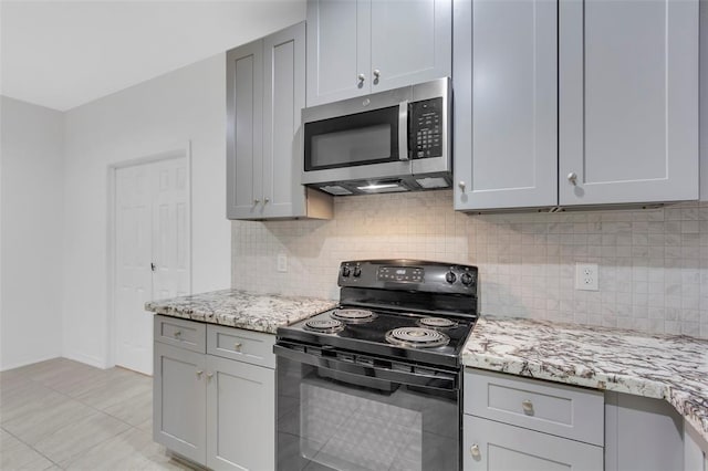 kitchen with gray cabinetry, black electric range oven, stainless steel microwave, tasteful backsplash, and light stone countertops