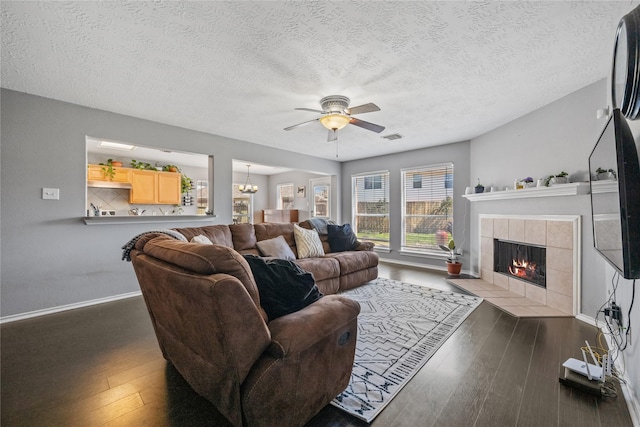 living room with visible vents, baseboards, wood-type flooring, a tiled fireplace, and ceiling fan with notable chandelier