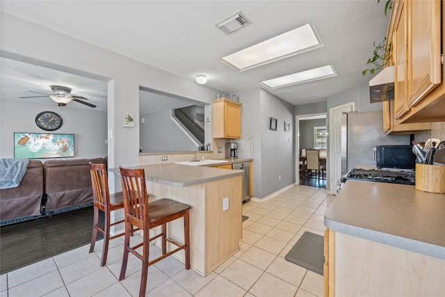 kitchen with backsplash, light tile patterned floors, appliances with stainless steel finishes, and light brown cabinetry