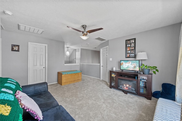 carpeted living room with visible vents, a textured ceiling, a ceiling fan, and a glass covered fireplace