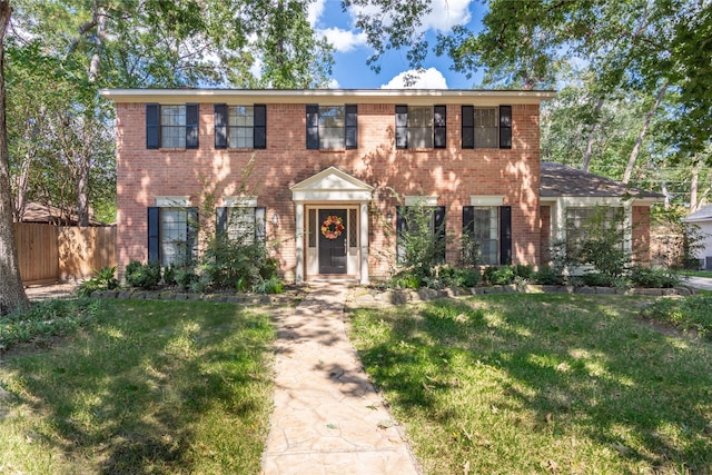 colonial inspired home featuring a front lawn, fence, and brick siding