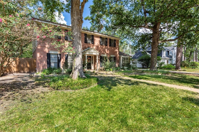 colonial house featuring brick siding, a front lawn, and fence