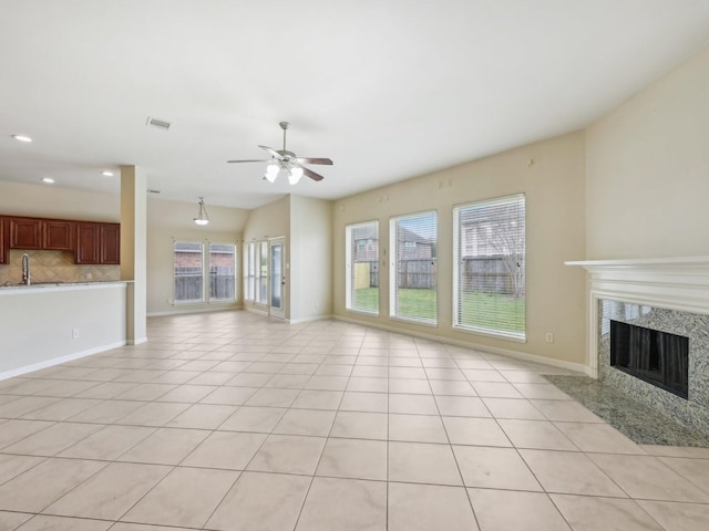 unfurnished living room featuring baseboards, visible vents, light tile patterned flooring, a fireplace, and a sink