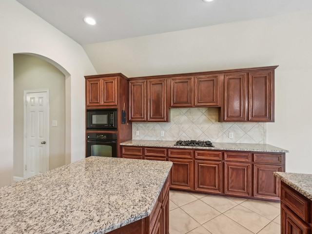 kitchen with decorative backsplash, black appliances, light stone counters, and arched walkways