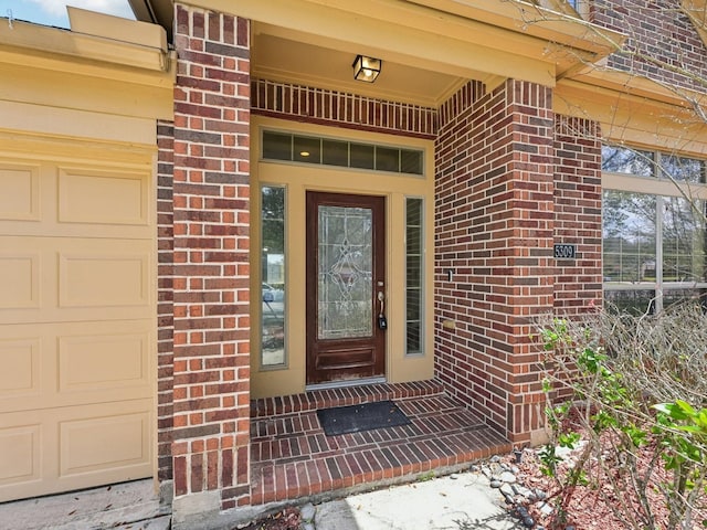 view of exterior entry featuring a garage and brick siding