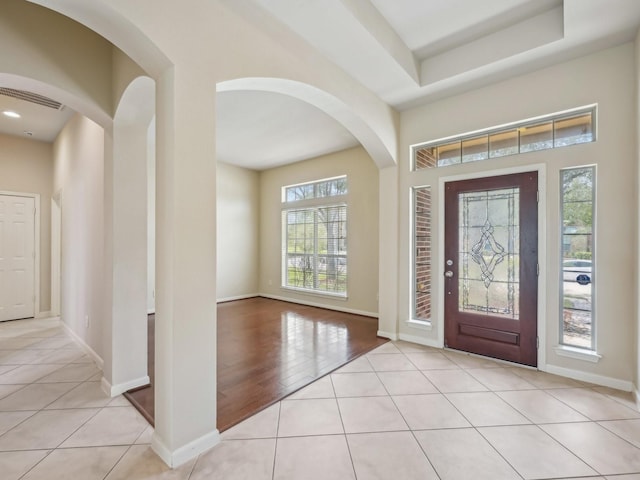 entryway with light tile patterned floors, a raised ceiling, and baseboards