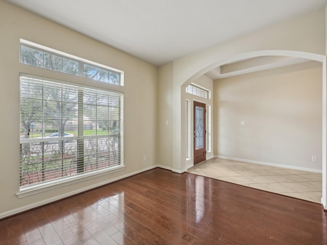 foyer featuring baseboards, arched walkways, and wood finished floors