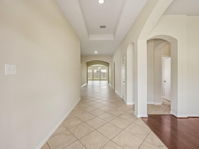 hallway featuring visible vents, recessed lighting, baseboards, arched walkways, and a raised ceiling