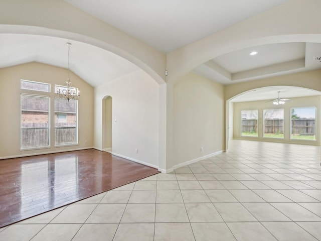 empty room with a tray ceiling, light tile patterned floors, ceiling fan with notable chandelier, and a wealth of natural light