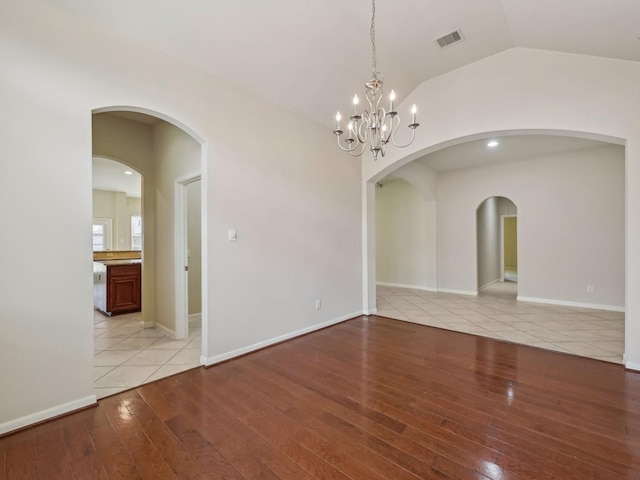 empty room featuring light wood finished floors, visible vents, baseboards, and vaulted ceiling