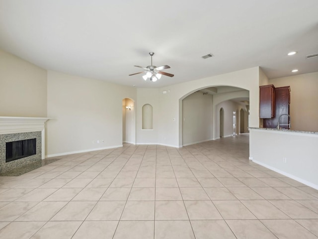 unfurnished living room with arched walkways, visible vents, a ceiling fan, and a premium fireplace