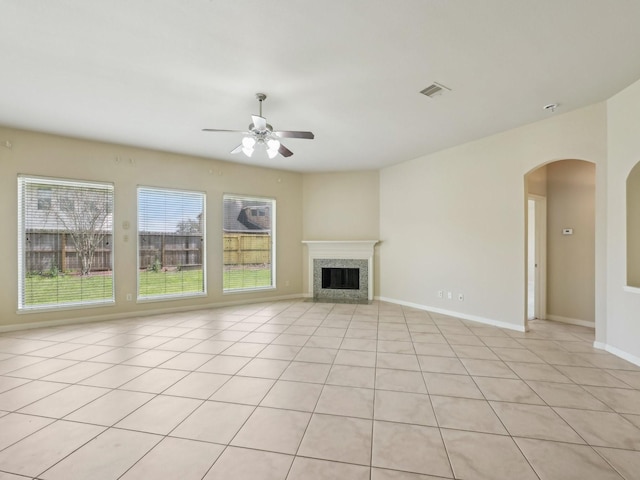 unfurnished living room featuring visible vents, a ceiling fan, arched walkways, a fireplace, and baseboards