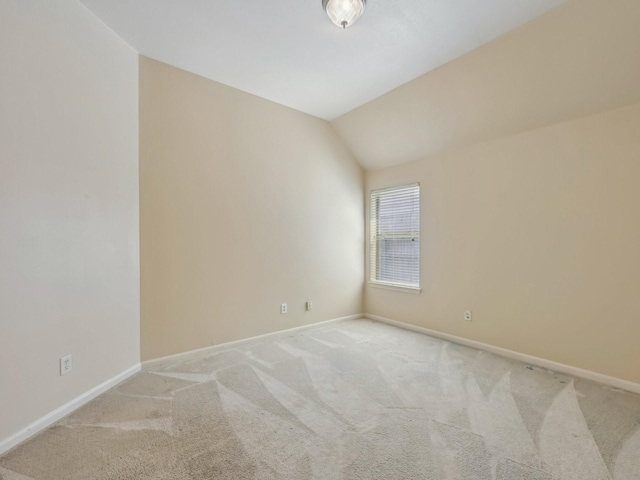 empty room featuring lofted ceiling, baseboards, and light carpet