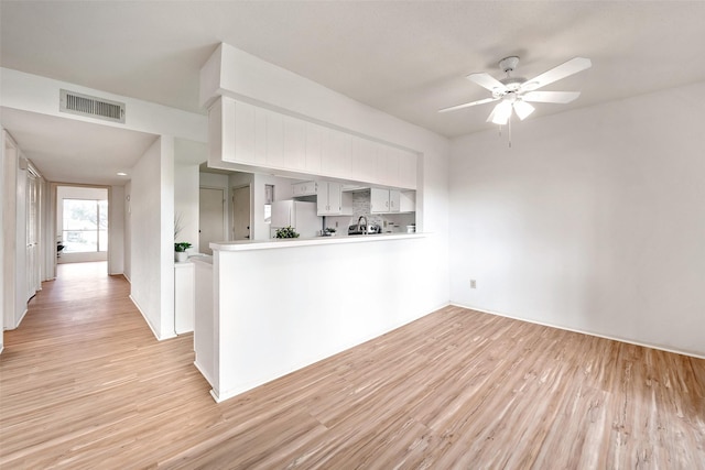 kitchen featuring visible vents, a peninsula, light wood-style flooring, and freestanding refrigerator