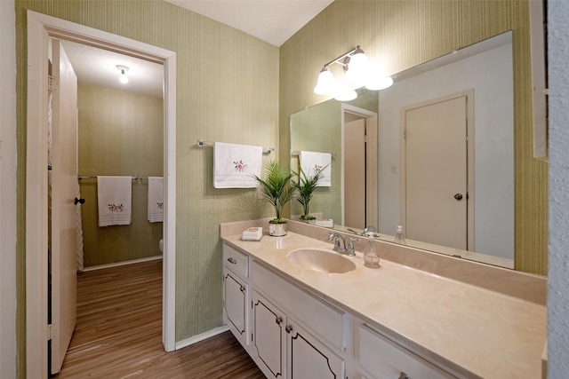 bathroom featuring wallpapered walls, baseboards, toilet, wood finished floors, and vanity