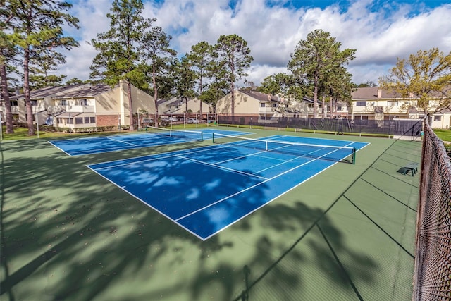 view of tennis court featuring community basketball court, fence, and a residential view