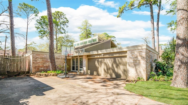 back of house with brick siding, an attached garage, concrete driveway, and fence