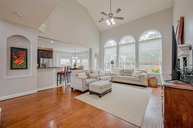 living area with baseboards, wood-type flooring, high vaulted ceiling, and ceiling fan with notable chandelier