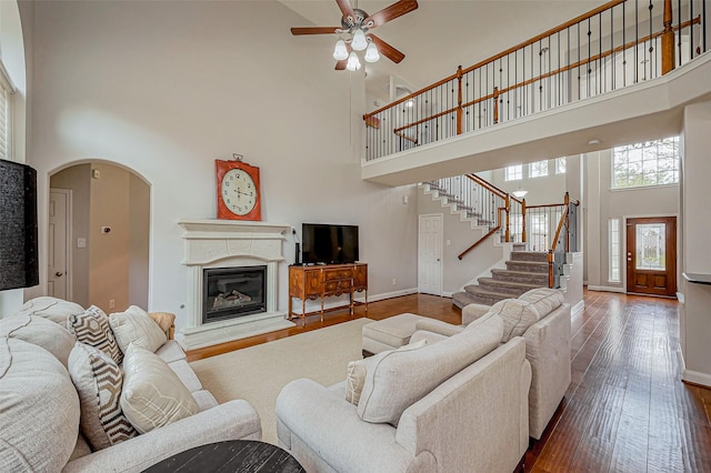 living area with a ceiling fan, hardwood / wood-style flooring, baseboards, a towering ceiling, and stairs