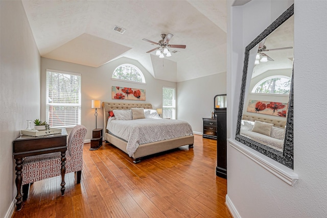 bedroom featuring visible vents, light wood-style flooring, a ceiling fan, baseboards, and vaulted ceiling