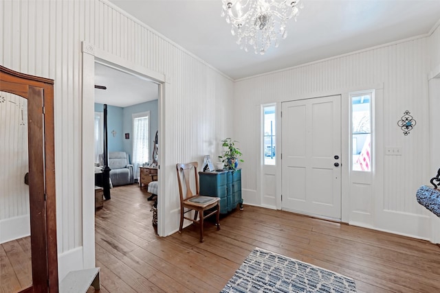 entryway with light wood-style flooring, a notable chandelier, and ornamental molding