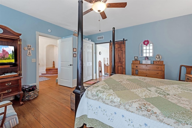 bedroom featuring a ceiling fan, visible vents, arched walkways, hardwood / wood-style flooring, and a barn door