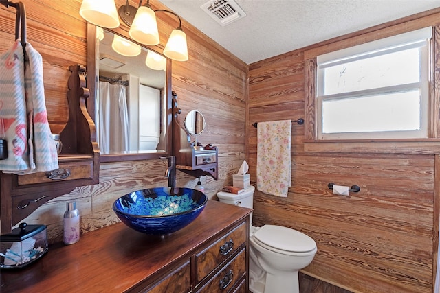 full bathroom featuring vanity, wooden walls, visible vents, a textured ceiling, and toilet