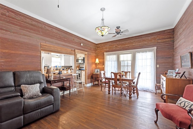 dining space featuring ceiling fan, wooden walls, and dark wood-style floors