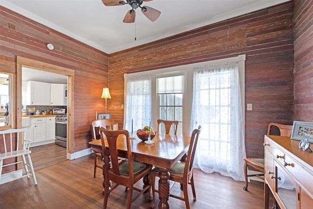 dining room featuring dark wood-style floors, a ceiling fan, and wood walls