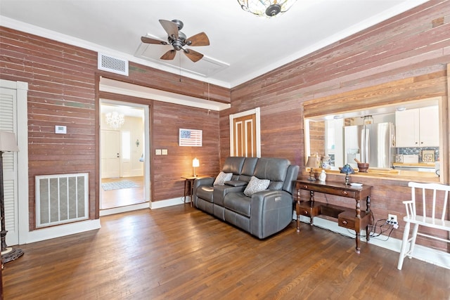 living room featuring dark wood finished floors, a ceiling fan, visible vents, and wood walls