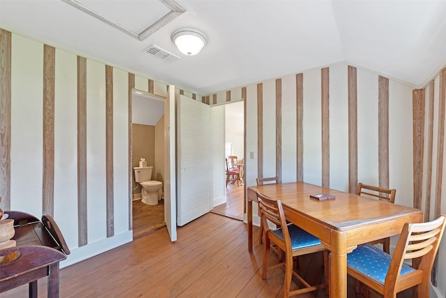 dining room with visible vents, wallpapered walls, light wood-style floors, and vaulted ceiling