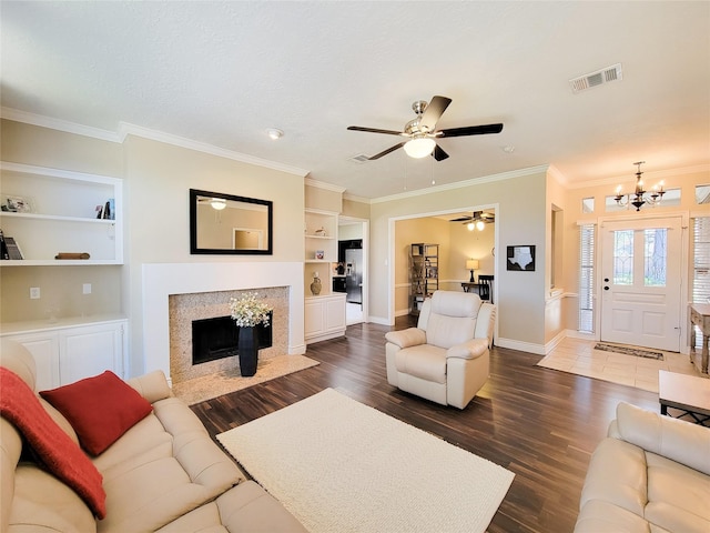 living area with built in features, wood finished floors, visible vents, a fireplace with flush hearth, and crown molding