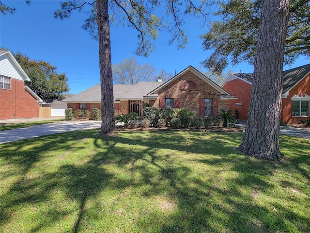 ranch-style home featuring driveway, brick siding, a chimney, and a front lawn