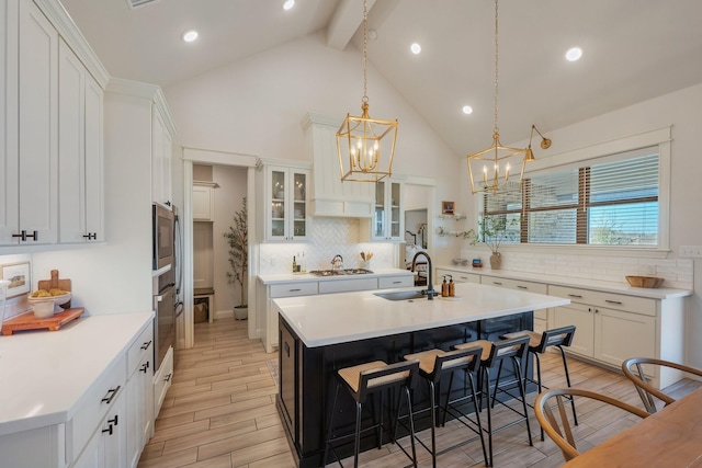 kitchen with wood finish floors, a kitchen island with sink, a sink, stainless steel appliances, and light countertops