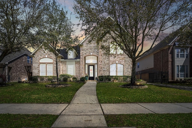 french country inspired facade with stone siding and a lawn