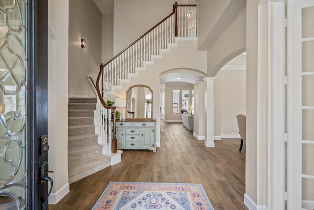 entryway with dark wood finished floors, stairway, arched walkways, baseboards, and ornate columns