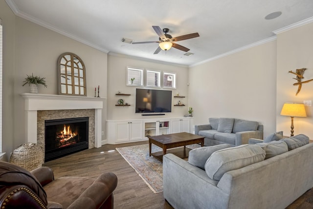 living area with visible vents, ornamental molding, a warm lit fireplace, dark wood-style floors, and ceiling fan