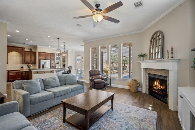 living area with visible vents, a tiled fireplace, dark wood finished floors, ornamental molding, and a ceiling fan