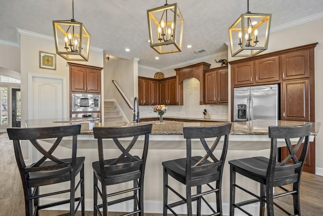 kitchen featuring an inviting chandelier, a kitchen island with sink, backsplash, and stainless steel appliances