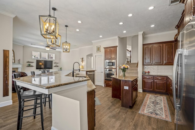 kitchen featuring dark wood-style floors, ceiling fan with notable chandelier, appliances with stainless steel finishes, a large island, and a sink