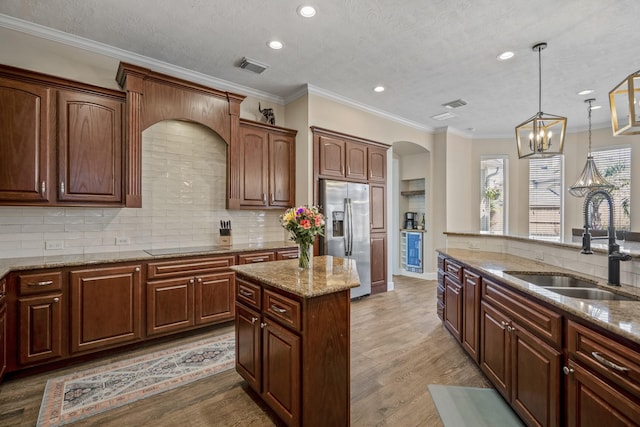 kitchen with pendant lighting, light wood-style flooring, stainless steel refrigerator with ice dispenser, a sink, and arched walkways