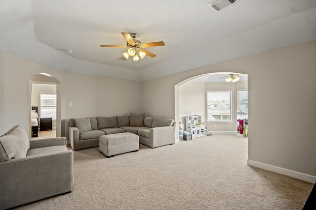 carpeted living area featuring a ceiling fan, visible vents, baseboards, arched walkways, and a raised ceiling