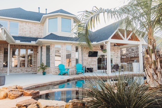 rear view of property with ceiling fan, an outdoor pool, a shingled roof, and a patio