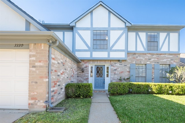 entrance to property featuring a yard, an attached garage, brick siding, and stucco siding