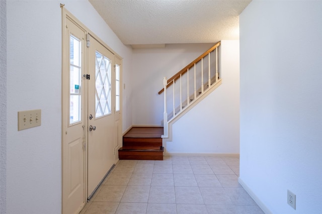 entryway featuring stairs, light tile patterned flooring, baseboards, and a textured ceiling