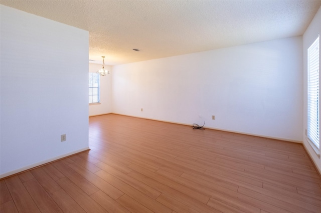 unfurnished room featuring visible vents, baseboards, a chandelier, light wood-style floors, and a textured ceiling