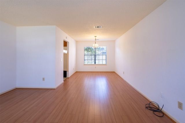 unfurnished room with visible vents, light wood-style floors, a chandelier, and a textured ceiling