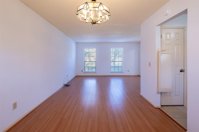 unfurnished room with an inviting chandelier, light wood-style floors, baseboards, and a textured ceiling